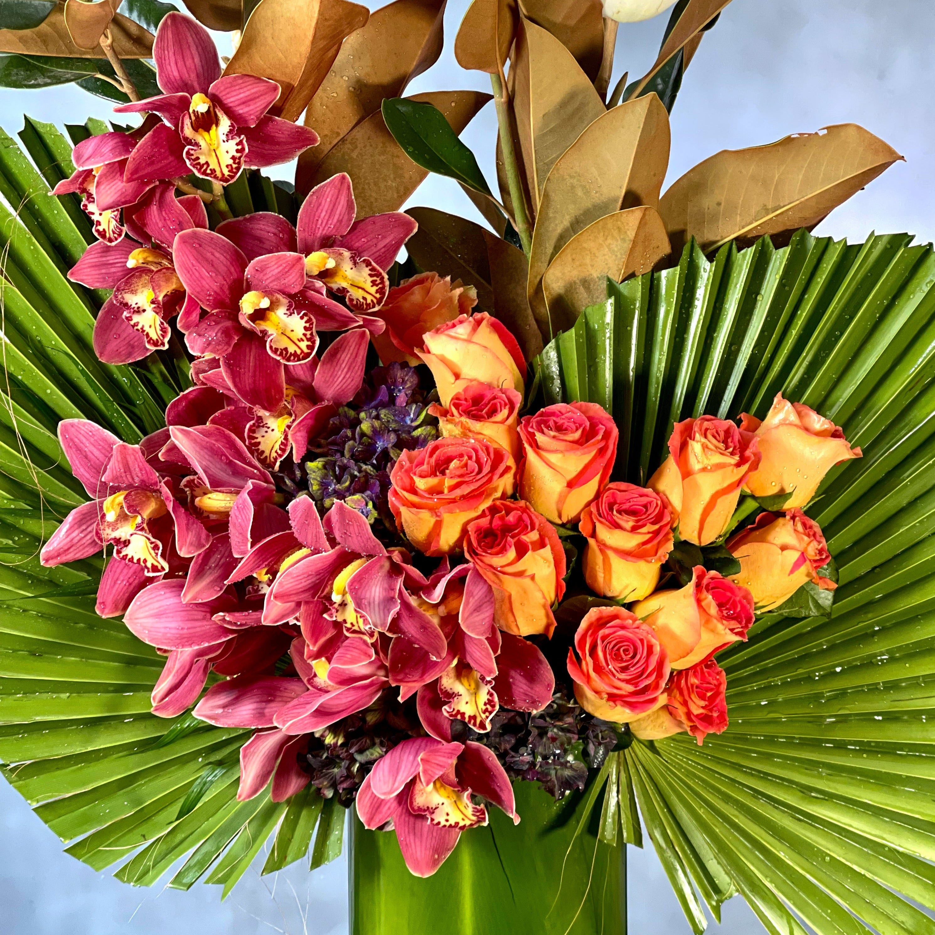 a-dream-come-true-tropical-orchids-roses-beverly-hills-florist.2 A Dream Come True arrangement with orange roses, cymbidium orchids, and fan palms in a tall glass vase, same-day delivery by Beverly Hills Florist.