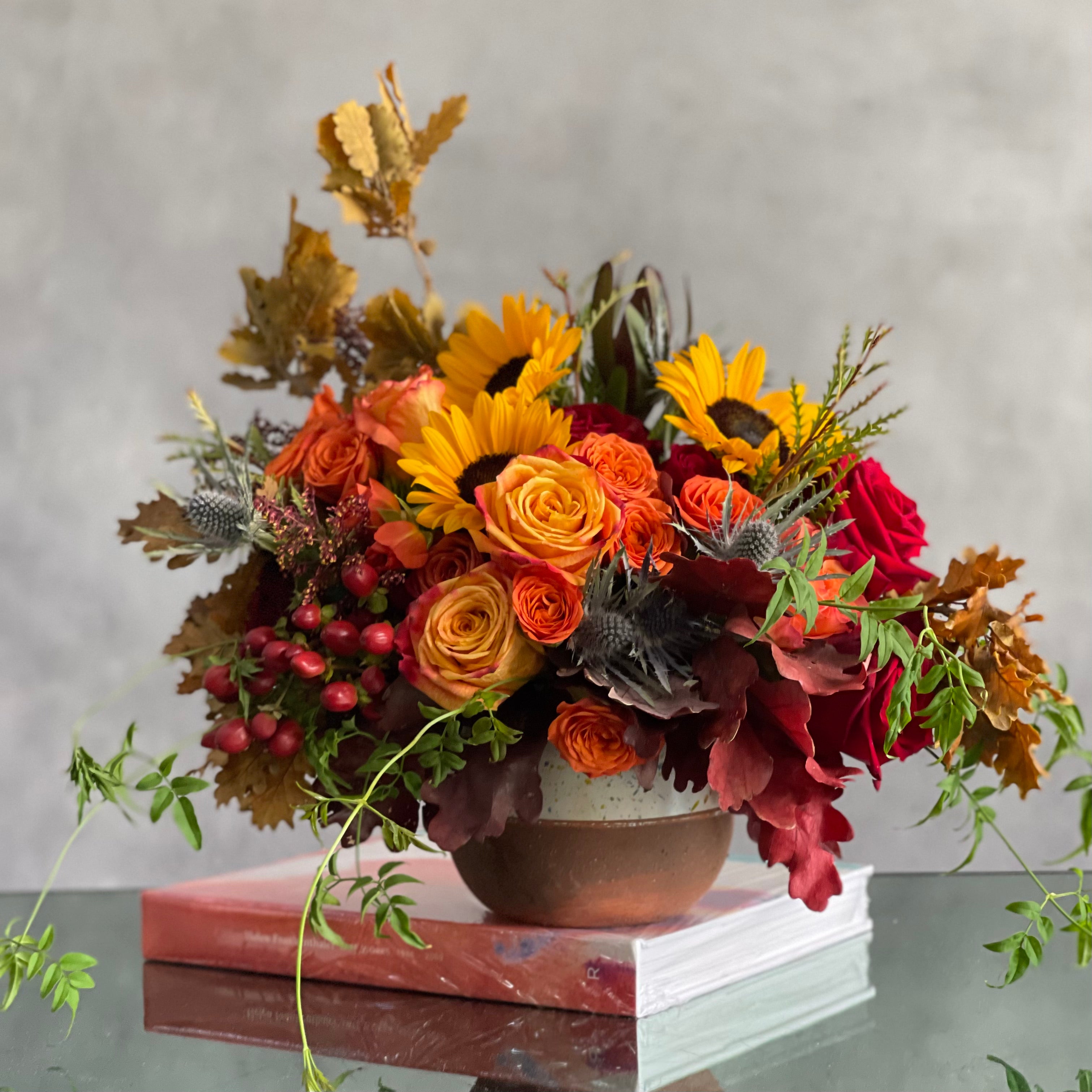 autumn-in-the-air-fall-flowers-sunflowers-90210-beverly-hills-florist.3 Autumn in the Air arrangement with orange, yellow, and red roses, sunflowers, and fall foliage in a ceramic vase, available for same-day delivery in 90210.