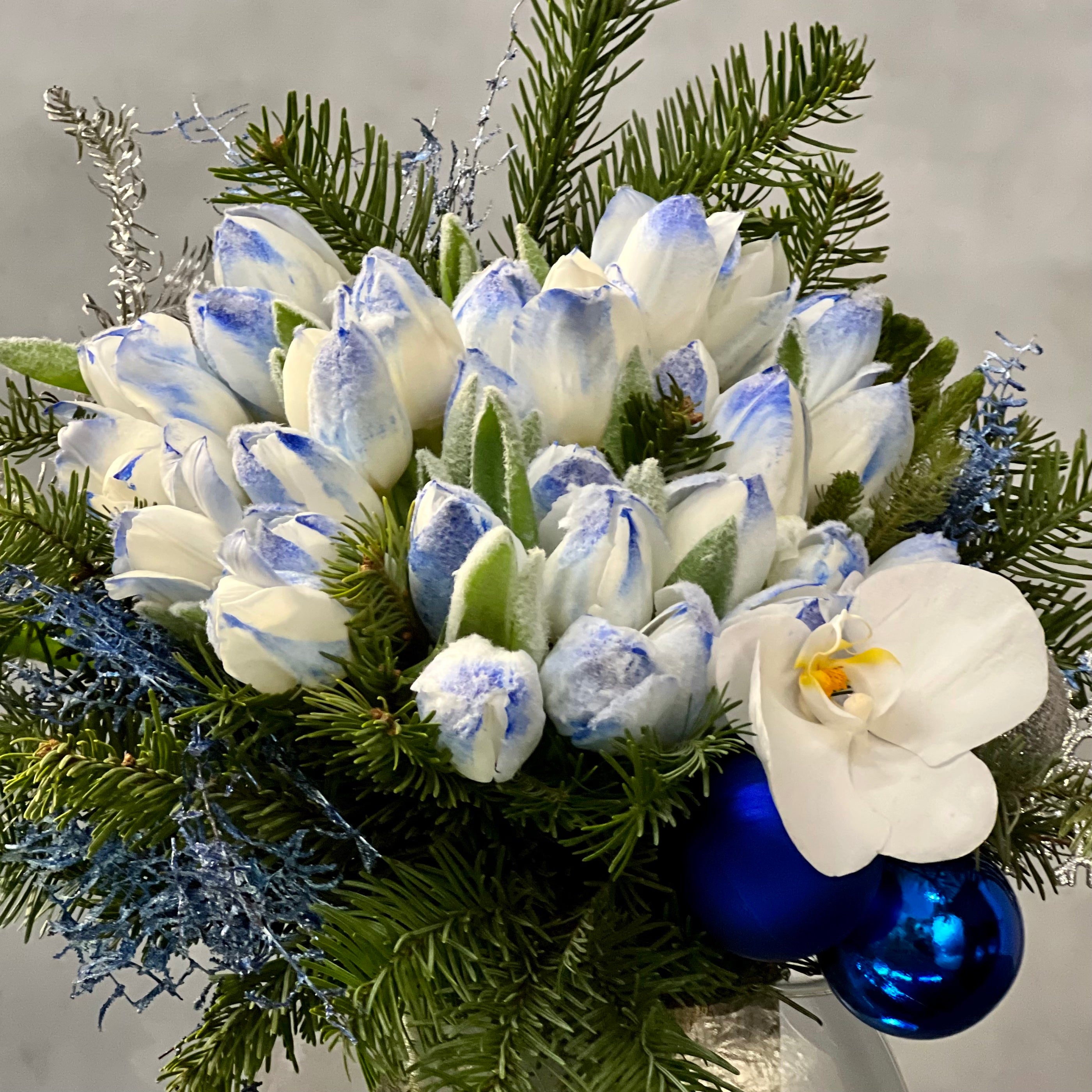 blue-holiday-designers-choice-tulips-orchid-bh-florist Blue Holiday arrangement with snow-tinted tulips and an orchid in a glass vase, available for same-day delivery by Beverly Hills Florist.