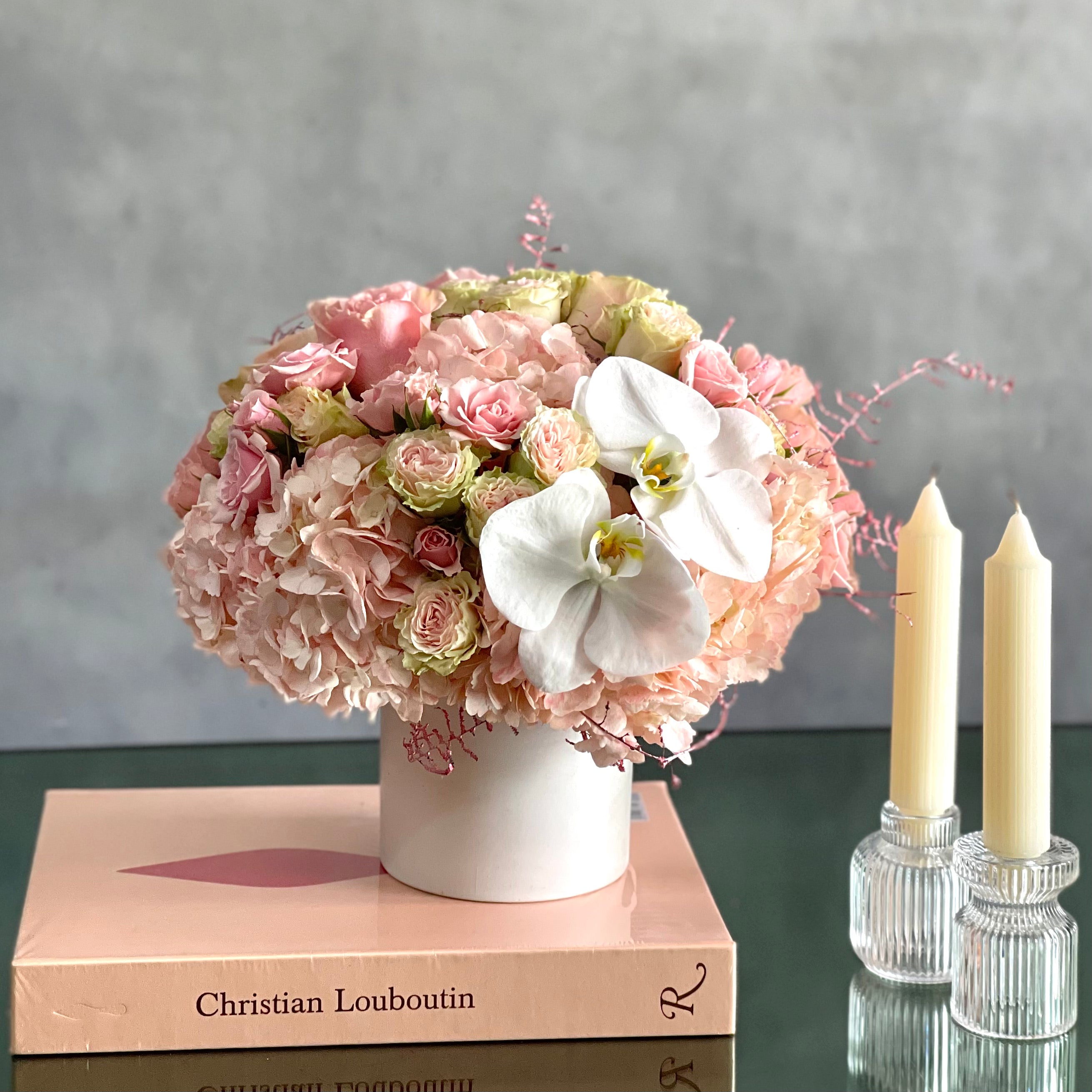 dancing-on-the-clouds-soft-pink-hydrangeas-white-orchids Dancing on the Clouds arrangement featuring soft pink hydrangeas, roses, spray roses, and white orchids in a chic white ceramic vase, perfect for all occasions.