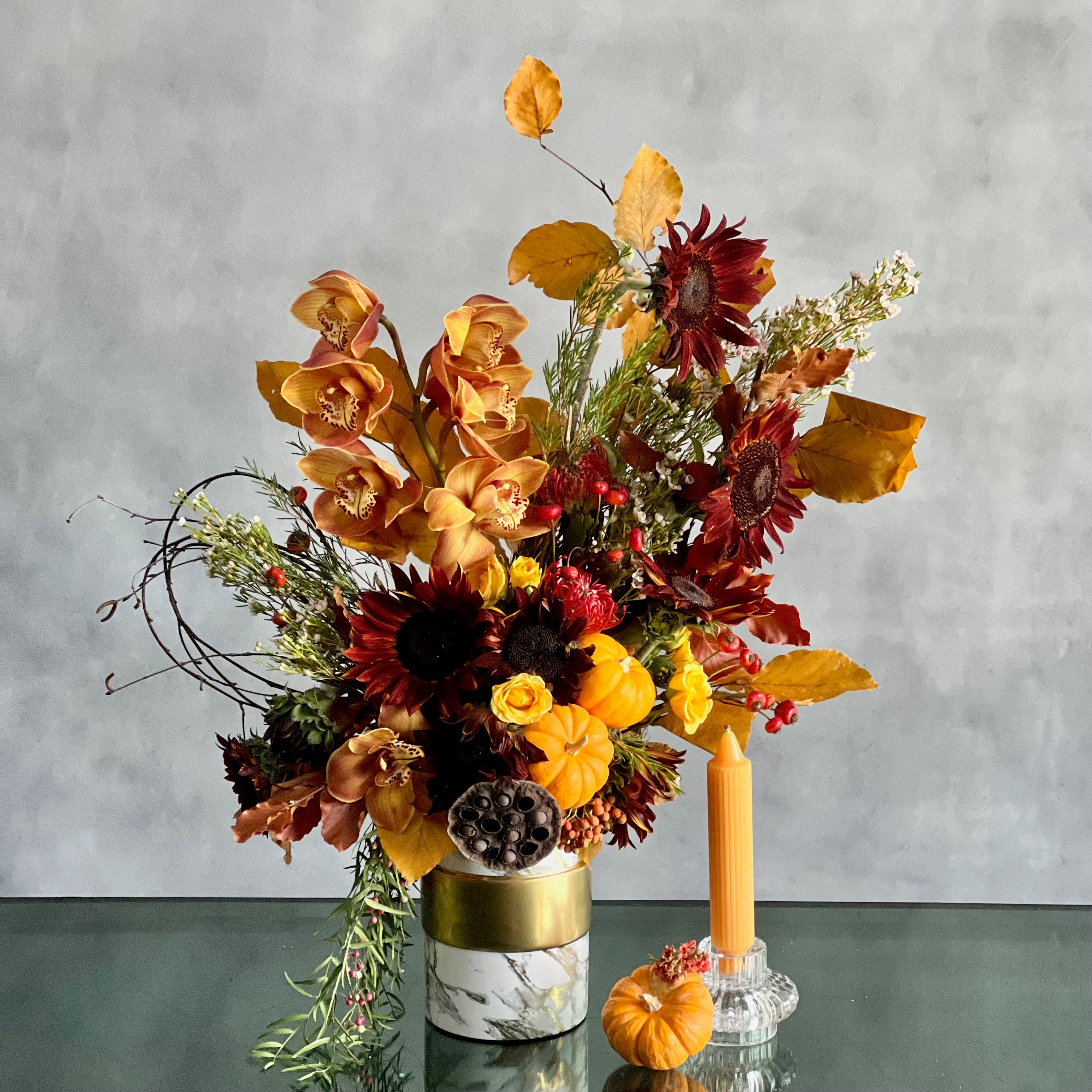 fallow-me-elegant-fall-orchids-black-sunflowers-pumpkins Elegant fall floral arrangement with Dutch Orchids, Black Sunflowers, berries, branches, fall foliage, mini pumpkins, and locally grown flowers in a marble gold container.