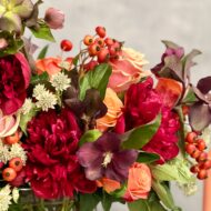 Majestic winter arrangement with orange roses, burgundy peonies, and winter accents in a glass vase – available for same-day delivery by Beverly Hills Florist.